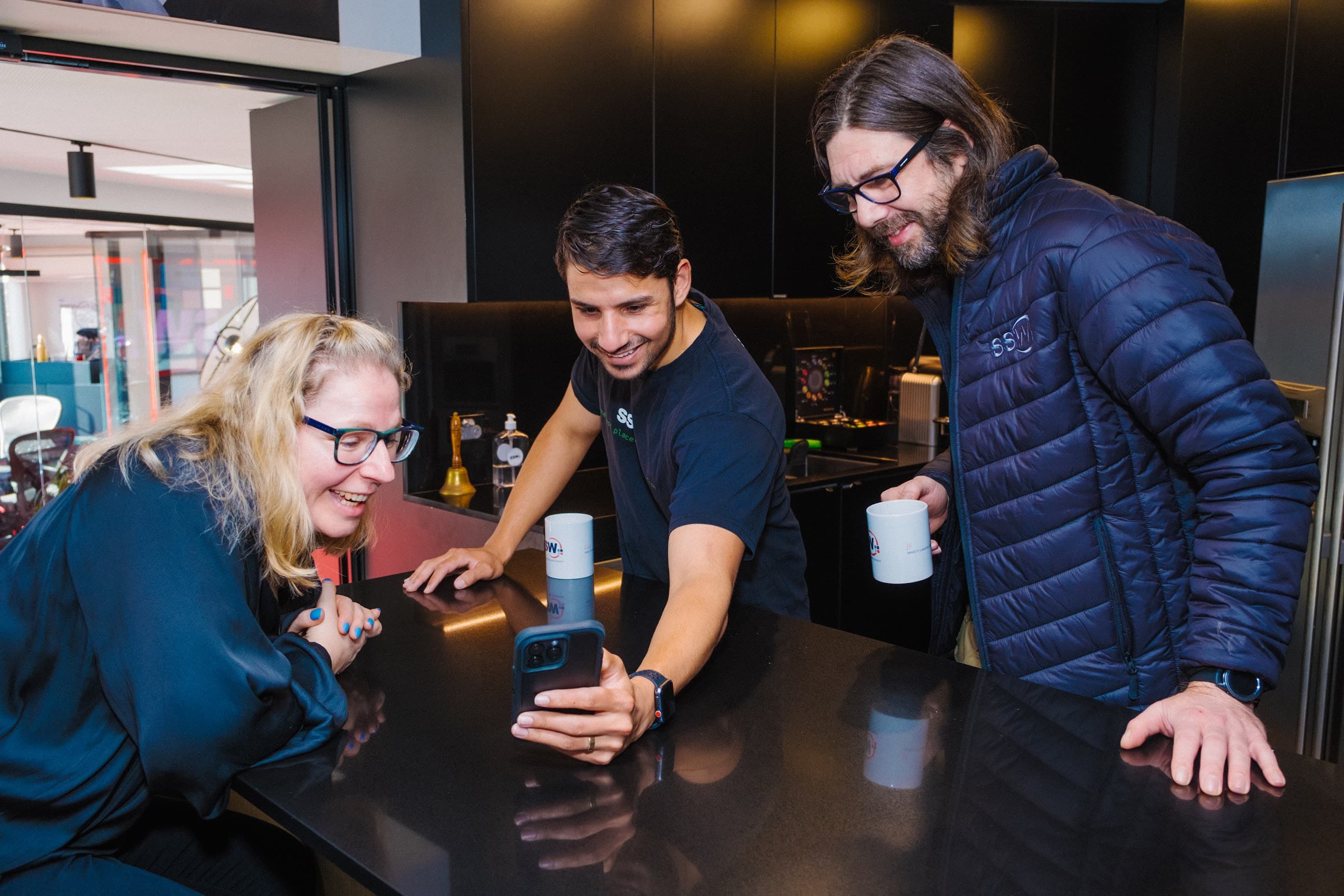 3 People looking at a mobile phone and smiling 